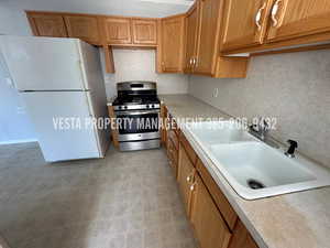 Kitchen with freestanding refrigerator, light countertops, brown cabinets, stainless steel range with gas cooktop, and light flooring