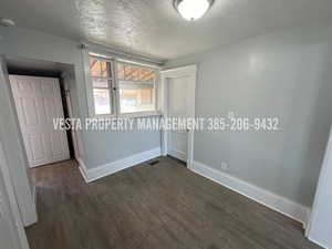 Empty room with a textured ceiling, dark wood-style floors, and a smoke detector