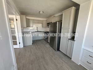 Kitchen with gray cabinetry, dark countertops, appliances with stainless steel finishes, a textured ceiling, and light wood finished floors