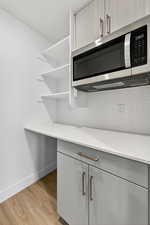 Kitchen view of stainless steel microwave, light wood finished floors, tasteful backsplash, and light stone counters