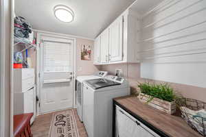 Washroom featuring a textured ceiling, cabinet space, light wood-style flooring, and washer and dryer