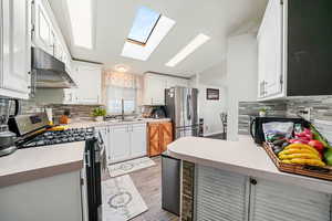 Kitchen with decorative backsplash, appliances with stainless steel finishes, a skylight, and white cabinets