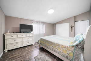 Bedroom with a textured ceiling, vaulted ceiling, dark wood-type flooring, and multiple closets