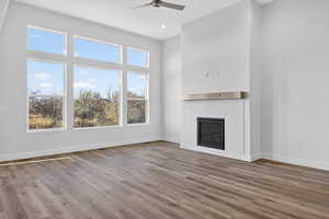 Unfurnished living room featuring a tile fireplace, wood finished floors, a ceiling fan, a towering ceiling, and recessed lighting