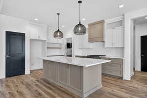 Kitchen featuring hanging light fixtures, a center island with sink, custom range hood, white cabinetry, and recessed lighting