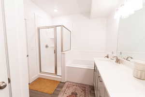 Full bath with vanity, a stall shower, a bath, and dark wood-type flooring