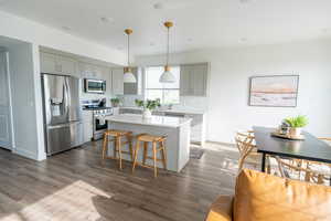 Kitchen featuring stainless steel appliances, decorative light fixtures, a breakfast bar, a kitchen island, and gray cabinetry