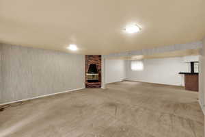 Below grade area with wallpapered walls, a brick fireplace, and light carpet