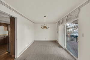 Unfurnished dining area featuring ornamental molding, a chandelier, and carpet flooring