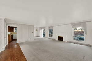 Unfurnished living room with ornamental molding, wood finished floors, wallpapered walls, a fireplace with flush hearth, and plenty of natural light