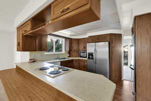 Kitchen featuring stainless steel appliances, light countertops, open shelves, and a peninsula