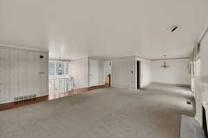 Unfurnished living room with a chandelier, carpet, wallpapered walls, ornamental molding, and a fireplace with flush hearth
