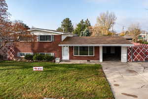 Split level home featuring brick siding, concrete driveway, a front yard, and a carport