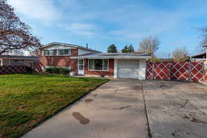 Split level home with brick siding, concrete driveway, a garage, and a gate