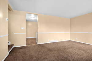 Carpeted empty room featuring baseboards and stairway