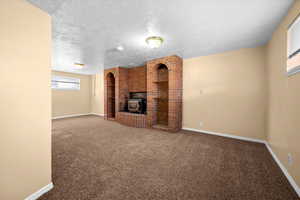 Unfurnished living room featuring a wood stove, carpet, and a textured ceiling
