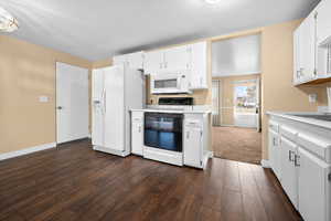 Kitchen featuring white appliances, white cabinets, light countertops, and dark wood-type flooring