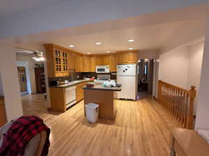 Kitchen featuring a kitchen island, recessed lighting, white appliances, light wood-type flooring, and glass insert cabinets