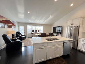 Kitchen with open floor plan, dark wood flooring, vaulted ceiling, appliances with stainless steel finishes, and kitchen island