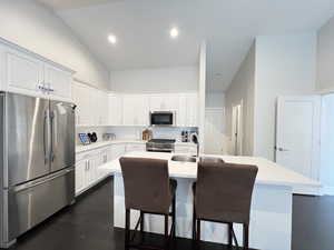 Kitchen featuring stainless steel appliances, high vaulted ceiling, a kitchen island with sink, a breakfast bar area, and white cabinets