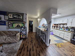 Kitchen with white cabinetry, a breakfast bar, light stone countertops, tasteful backsplash, and dark wood-style flooring