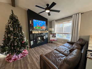 Living area with vaulted ceiling, a textured ceiling, wood finished floors, a fireplace, and ceiling fan