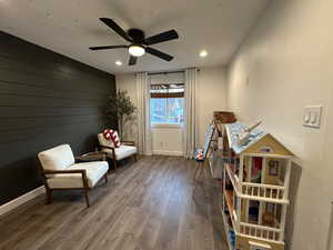 Sitting room with wood-type flooring, wood walls, ceiling fan, recessed lighting, and an accent wall