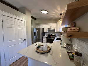 Kitchen featuring decorative backsplash, stainless steel appliances, pendant lighting, white cabinets, and a peninsula
