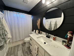 Bathroom with vanity, wood tiled floors, a textured ceiling, shower / bath combination with curtain, and wooden walls