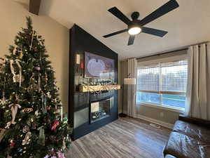 Unfurnished living room with lofted ceiling, a textured ceiling, wood finished floors, a ceiling fan, and a large fireplace