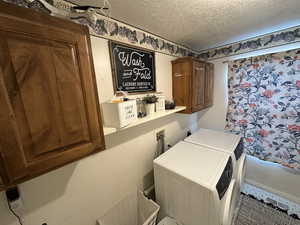 Laundry room with cabinet space, a textured ceiling, and separate washer and dryer