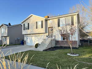 Split foyer home featuring concrete driveway, a front yard, a garage, and brick siding