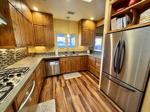 Kitchen with appliances with stainless steel finishes, brown cabinets, pendant lighting, dark wood finished floors, and recessed lighting