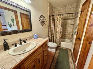 Full bath featuring vanity, a textured wall, shower / bath combo with shower curtain, and dark tile patterned floors
