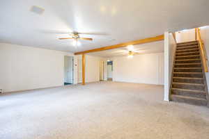Unfurnished living room featuring stairs, light carpet, and a ceiling fan