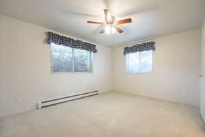 Spare room featuring baseboard heating, light colored carpet, plenty of natural light, and ceiling fan