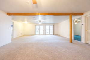 Unfurnished living room featuring ceiling fan, light colored carpet, beam ceiling, a textured ceiling, and baseboard heating