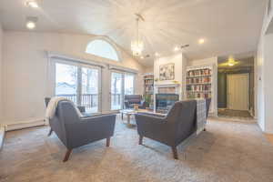 Living area featuring lofted ceiling, a tiled fireplace, a chandelier, built in shelves, and light carpet