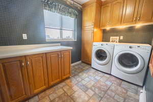 Laundry room featuring wallpapered walls, cabinet space, stone finish flooring, and independent washer and dryer
