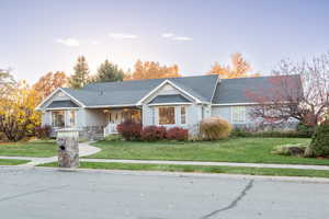 View of front of house featuring covered porch, a front yard, a shingled roof, and stone siding