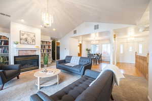 Living area featuring a chandelier, a fireplace, lofted ceiling, built in features, and light wood finished floors