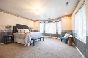 Carpeted bedroom featuring wallpapered walls, wainscoting, a chandelier, baseboard heating, and a textured ceiling