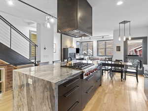Kitchen with hanging light fixtures, modern cabinets, dark brown cabinets, a kitchen island, and light wood-style flooring