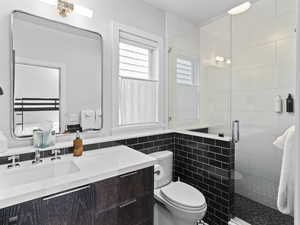 Bathroom featuring vanity, a shower stall, and tile walls