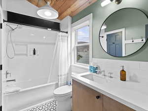 Full bath with wooden ceiling, vanity, shower / bath combo with shower curtain, tile walls, and a wainscoted wall
