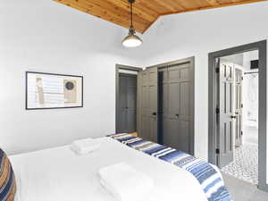 Bedroom with vaulted ceiling, a closet, wood ceiling, ensuite bath, and carpet floors