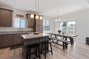 Kitchen featuring pendant lighting, light wood-style flooring, light stone countertops, a kitchen bar, and healthy amount of natural light