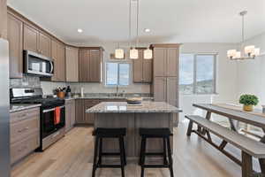 Kitchen with appliances with stainless steel finishes, light stone countertops, decorative light fixtures, a kitchen breakfast bar, and recessed lighting