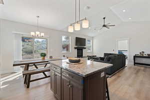 Kitchen featuring light stone countertops, dark brown cabinets, pendant lighting, a fireplace with raised hearth, and vaulted ceiling
