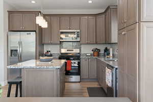 Kitchen featuring stainless steel appliances, light stone countertops, a center island, pendant lighting, and light wood-type flooring